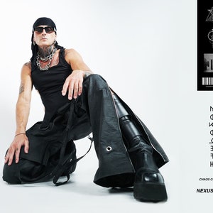May include: A person wearing a black tank top, black pants with a zipper detail, and black boots. The person is wearing a black bandana and sunglasses. The image also includes text that reads "Chaos Coalesce Nexus Pant".