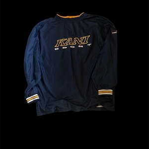 May include: A navy blue long-sleeve pullover jacket featuring the text KANI SPORT embroidered in yellow and white on the chest. The garment has a yellow collar trim and striped yellow and white cuffs at the wrists, with a small KANI logo tag.