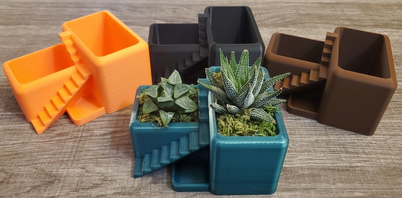 May include: A collection of geometric planters in various colors, including orange, teal, brown, and black. Each planter features a staircase design and holds small succulents with green moss.