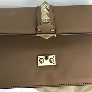 Op de afbeelding: Een bruinleren clutch met een klepsluiting. De clutch heeft goudkleurige piramidevormige studs aan de voorkant en een goudkleurige sluiting. De tas is rechthoekig en heeft een gestikte rand.