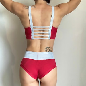 Puede incluir: Top deportivo rojo y blanco con un detalle blanco en forma de cruz en la espalda y pantalones cortos deportivos a juego rojo y blanco.