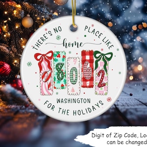 May include: A white ceramic Christmas ornament with the text "There's no place like home" and "Washington for the holidays." The ornament features a design with the numbers "8062" in a festive style, with bows and patterns.