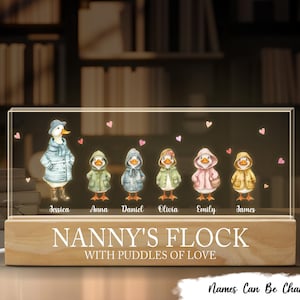May include: A personalised night light with a wooden base and acrylic front, depicting a family of ducks in raincoats. The base reads "Nanny's Flock with Puddles of Love." Names are printed below each duck, with customisation available.
