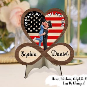 May include: A wooden heart-shaped ornament with a couple kissing, set against an American flag design. The words "YOU AND ME" and "WE GOT THIS" are displayed. The names "Sophia" and "Daniel" are also included. The text "Name, Skintone, Outfit & Hairstyle Can Be Changed" is also visible.