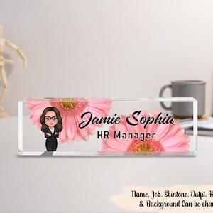 May include: A clear acrylic desk block with the name "Jamie Sophia" and the title "HR Manager" in black script. The design includes a cartoon image of a person and pink gerbera daisies.