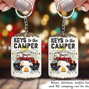 May include: A pair of personalized keychains with the text "KEYS to the CAMPER" and a cartoon image of a couple sitting by a campfire with an RV in the background. The keychains are on a wooden background.