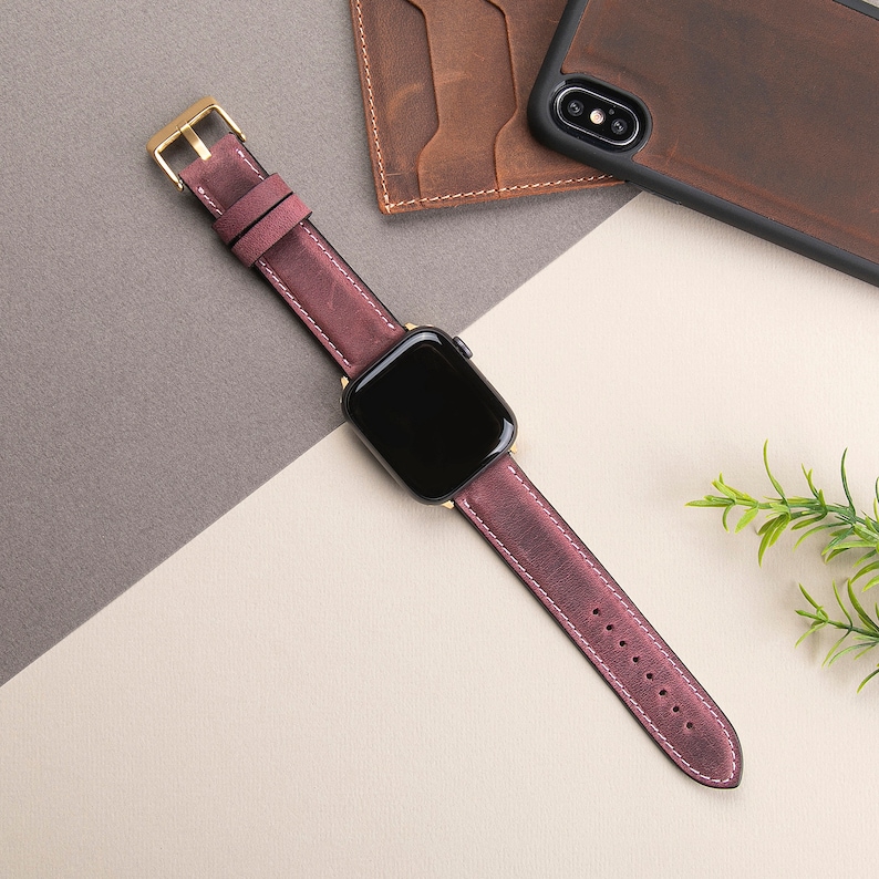 May include: A burgundy leather watch band with gold hardware and a black watch face.