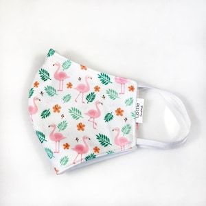 May include: White face mask with a pink flamingo and green leaf pattern. The mask has a white elastic band and a white label that says "Lottie Handmade".