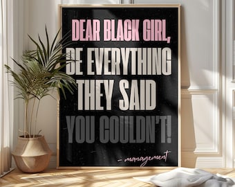 May include: A framed art print with the text "DEAR BLACK GIRL, BE EVERYTHING THEY SAID YOU COULDN'T!" in pink, white, and gray on a black background. The print is in a gold frame and is displayed in a room with a plant and wooden floor.