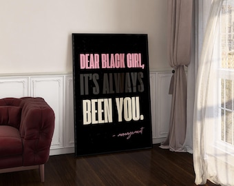 May include: A black framed poster with the text "DEAR BLACK GIRL, IT'S ALWAYS BEEN YOU." in pink, gray, and white. The word "management" is written below the text. A burgundy sofa is visible on the left.