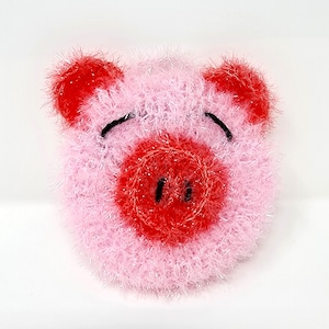 May include: A pink, fluffy pig face with red ears and snout. The pig has black eyes and nostrils. The material has a sparkly, textured appearance. The pig is a whimsical, handmade item.