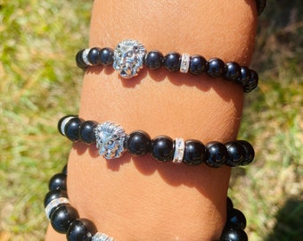 May include: Four black beaded bracelets with silver lion head charms. Each bracelet has a row of small clear rhinestones.