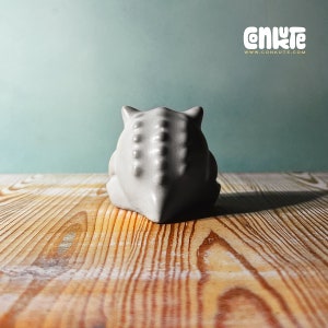 May include: A white ceramic sculpture of a creature with a spiky back, sitting on a wooden surface.