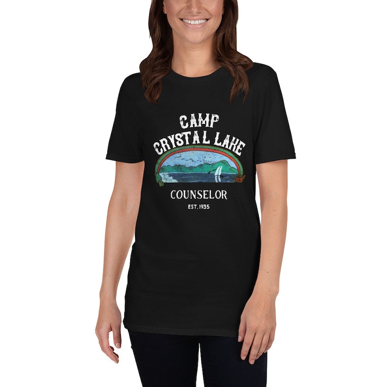 Pu&ograve; includere: T-shirt nero con una grafica bianca di un logo in stile vintage per Camp Crystal Lake. Il logo presenta un lago con una montagna sullo sfondo, un arcobaleno e il testo "Camp Crystal Lake Counselor Est. 1955".