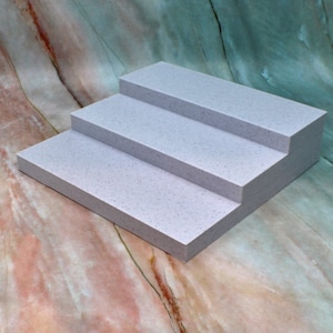 May include: Three white steps made of a textured material, arranged in a staircase formation on a marble background.