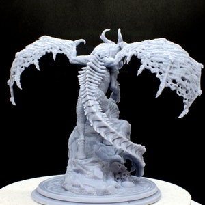 Puede incluir: Una miniatura de drag&oacute;n gris impresa en 3D con las alas extendidas, posada sobre una base rocosa. El drag&oacute;n tiene una cola puntiaguda detallada y un cuerpo &oacute;seo texturizado.