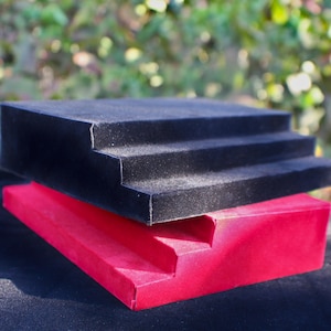 May include: A black velvet tiered display stand with three steps, stacked on top of a red velvet tiered display stand with two steps.