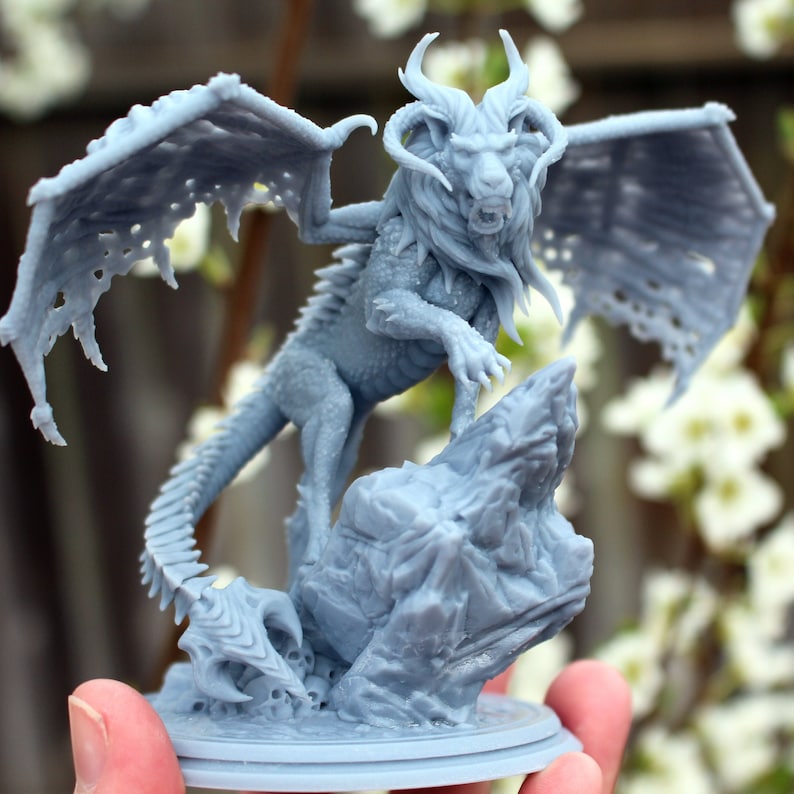 A large 3D print of a manticore monster held up by a human hand against a backdrop of flowers.