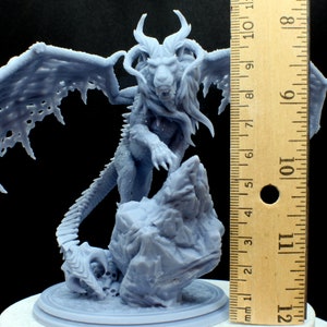 Puede incluir: Una miniatura gris de un le&oacute;n alado con una base rocosa, impresa en 3D. La miniatura mide aproximadamente 15 cm de alto.