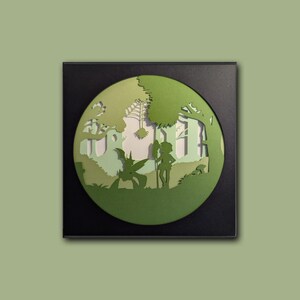 May include: A framed paper cut artwork depicting a layered forest scene in various shades of green. The circular design showcases silhouettes of trees, a fairy-like creature, and a figure with a staff, set against a light green backdrop.