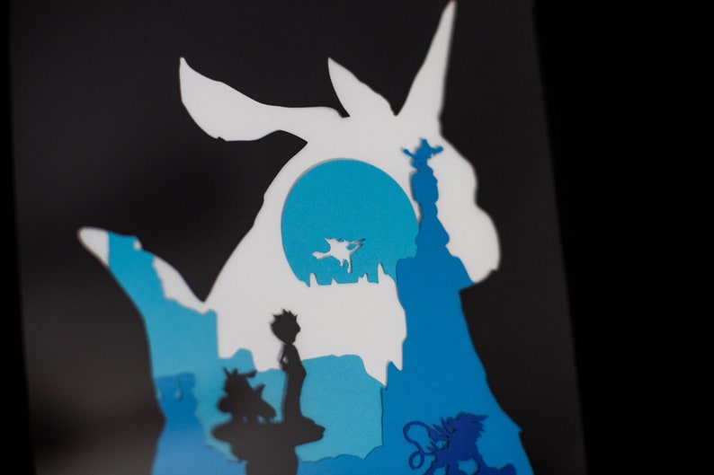 May include: Paper cut-out art depicting a blue and white silhouette of a Pokemon character, with a blue moon in the background. The character is surrounded by other smaller cut-out figures, including a person and a small animal.