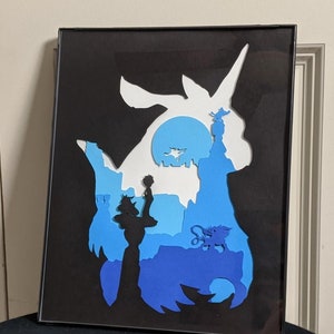 May include: A framed paper art piece depicting a blue and white silhouette of a mythical creature with a unicorn horn. The creature is surrounded by a blue and white landscape with a small figure standing on a tower.