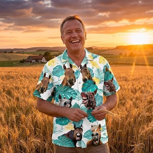 May include: A short-sleeved button-down shirt with a white background, featuring a pattern of horse faces and green tropical leaves. The shirt is worn by a person standing in a wheat field at sunset.