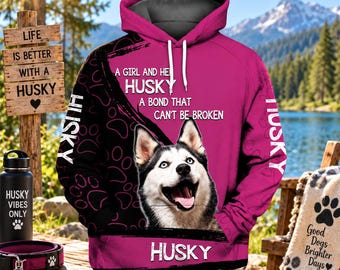May include: A pink and black hooded sweatshirt featuring a graphic of a Husky dog, the text A GIRL AND HER HUSKY A BOND THAT CAN'T BE BROKEN, and the word HUSKY printed on the front. The hoodie includes white drawstrings and a patterned paw print design.