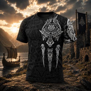 May include: A black short-sleeve t-shirt featuring a white graphic print of a stylized wolf head and three vertical dagger-like symbols on the front. The fabric is covered in a dark grey intricate woven knotwork pattern across the entire surface.