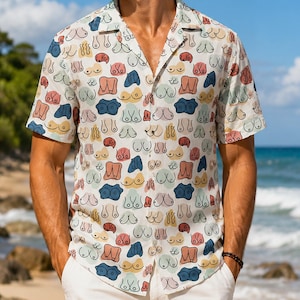 May include: Short-sleeved button-down shirt with a white background and a repeating pattern of colorful, abstract breast illustrations. The shirt has a classic collar and is worn with white pants. The overall style is casual and beachy.