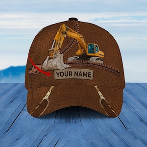 Puede incluir: Gorra de béisbol de cuero marrón con un diseño de excavadora amarilla y el texto "YOUR NAME" en la parte delantera.