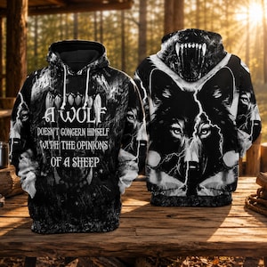 Könnte beinhalten: Ein schwarz-weißer Kapuzenpullover mit einer Grafik eines Wolfsgesichts und Blitzen. Auf der Vorderseite steht der Text: A WOLF DOESN'T CONCERN HIMSELF WITH THE OPINIONS OF A SHEEP. Die Kapuze zeigt das geöffnete Maul eines Wolfs mit Zähnen.
