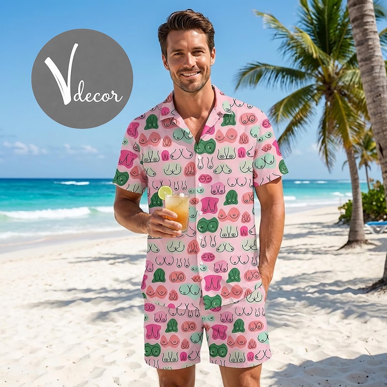 May include: Pink button-down shirt and matching shorts set with a repeating pattern of stylized breasts in various colors. The outfit is worn on a beach setting, suggesting a casual, summer theme.