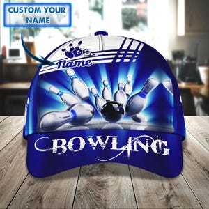 May include: A blue and white baseball cap with a bowling theme. The cap features a bowling ball and pins graphic, with the word "BOWLING" in white. The top of the cap has the text "CUSTOM YOUR NAME".