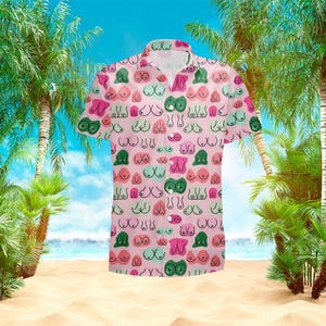 May include: A short-sleeved button-down shirt with a pink background and a repeating pattern of stylized breasts in various colors, including green, pink, and blue. The shirt has a classic collar and a relaxed fit, suitable for casual wear.