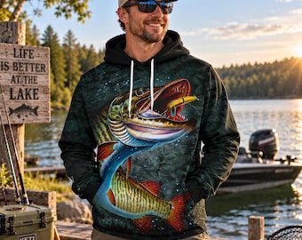 Può includere: Una felpa nera a maniche lunghe con cappuccio, caratterizzata da una grande grafica colorata di un pesce muskellunge che morde un'esca da pesca gialla. La felpa presenta un cappuccio con coulisse e un motivo scuro e maculato sul davanti.