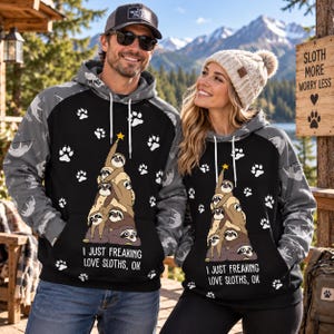 May include: Two matching black and grey hoodies featuring a graphic of sloths stacked in a tree shape with a yellow star on top. The text reads I JUST FREAKING LOVE SLOTHS, OK. The sleeves and hood are grey with a repeating sloth and paw print pattern.