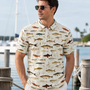 May include: A short-sleeved polo shirt in an off-white colour featuring an all-over print of various fish in shades of brown, orange, and green, with a classic collar, a buttoned placket, and a regular fit, worn with light-coloured trousers.