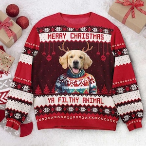 Op de afbeelding: Rode kersttrui met een hond met geweien en een feestelijke trui. De tekst "MERRY CHRISTMAS" en "YA FILTHY ANIMAL" zijn te zien. Het ontwerp bevat sneeuwvlokken en kerstbomen.