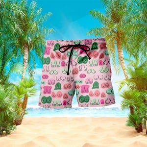May include: Pink swim trunks with a repeating pattern of stylized breasts in various colors. The shorts have a black drawstring and are set against a beach scene with palm trees and a blue sky.