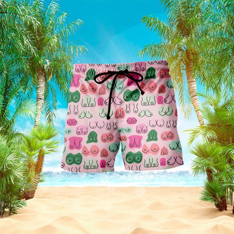 May include: Pink swim trunks with a repeating pattern of stylized breasts in various colors. The shorts have a black drawstring and are set against a beach scene with palm trees and a blue sky.
