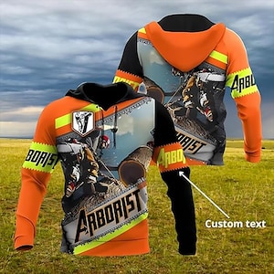 May include: Orange and black hooded sweatshirt with the word "ARBORIST" printed on the front and sleeves. The design features a lumberjack scene and a logo. The sleeves are black, and the hood is orange.