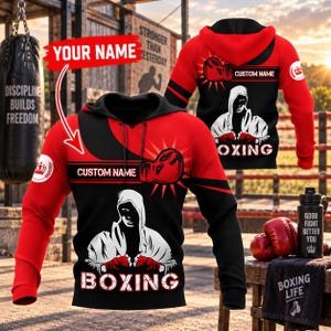 May include: A red and black hooded sweatshirt featuring a graphic of a hooded boxer, red boxing gloves, and the text "BOXING" and "CUSTOM NAME". The design includes a red arrow pointing to the chest area with the text "YOUR NAME".