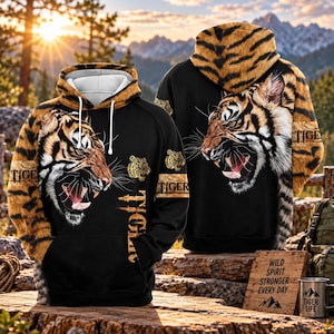 Op de afbeelding: Een zwarte hoodie met een grote, gedetailleerde afbeelding van een brullende tijger op de voor- en achterkant. De mouwen en capuchon hebben een tijgerstrepenpatroon. Het woord TIGER staat in een verweerd lettertype op de voorzijde. Witte koorden.