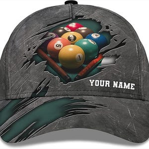 Puede incluir: Una gorra de béisbol gris con un aspecto desgastado. La parte delantera de la gorra presenta un diseño desgarrado que revela un grupo de bolas de billar con el texto "YOUR NAME" debajo.
