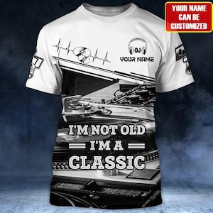 May include: A white short-sleeve t-shirt featuring a black and white graphic of a turntable and vinyl record. The text reads I'M NOT OLD I'M A CLASSIC. It includes a heartbeat line, headphones icon, and a box stating YOUR NAME CAN BE CUSTOMIZED.