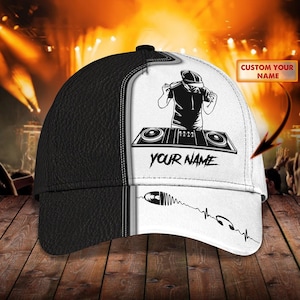 May include: Black and white baseball cap with a DJ graphic, a record player, and the text "YOUR NAME" on the front. The cap has a black leather bill and a white mesh back.