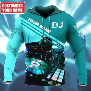 May include: Teal hoodie with a DJ theme. The front features a graphic of a DJ mixer and headphones. The text "YOUR NAME" and "DJ" are printed on the front. The top left corner has the text "CUSTOMIZED YOUR NAME" in a red box.