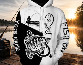 Può includere: Una felpa con cappuccio bianca e nera con un design diviso. La parte anteriore mostra la grafica di un pesce all'amo, una persona che pesca su una barca e il testo "FISH ON!" e "YOUR NAME". Le maniche riportano anche il testo "FISH ON".
