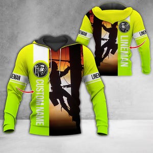 Pode incluir: Um moletom verde neon com um gráfico em preto e branco de um eletricista escalando um poste de utilidade. O moletom apresenta a palavra "LINEMAN" nas mangas e o texto "CUSTOM NAME" na frente. O fundo mostra um pôr do sol.